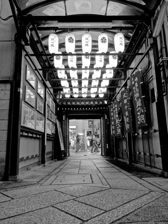 Along one of the covered pedestrian-only streets in Kyoto, the entrance to a Buddhist temple is lit up with paper lanterns.