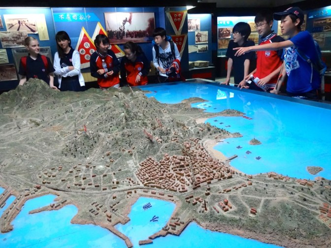Students explore a scale model of the Qingdao area depicting the city during a siege of the city by British and Japanese forces in October and November 1914.