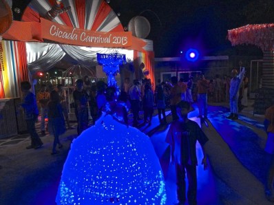 Alex stands next to a woman at the Orange Happiness New Year's festival, dressed in lighted neon blue dress.